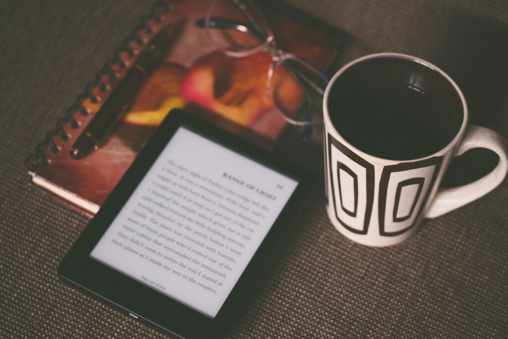 Dimmed image of a Kindle, journal and pen, and a warm beverage as part of an evening routine